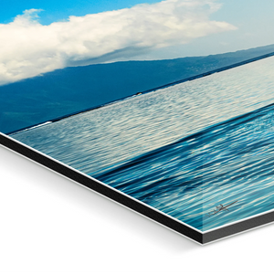 Close-up of plexiglass photo print featuring calm ocean, blue sky, and distant mountains