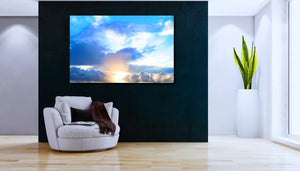 Modern living room with large sunrise sky photography wall art, cozy white chair, and potted plant.