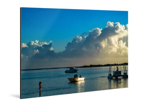 Glossy aluminum photo print of a waterfront scene with boats, clouds, and a child wading.