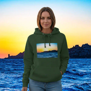 Woman in green hoodie with sunset seascape print, standing by ocean at dusk