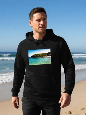 Man wearing black hoodie with beach landscape print, walking on sandy ocean shore