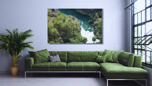 Modern living room with green sofa, large landscape wall art, indoor plant, and tall windows