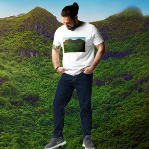 Man in white t-shirt with mountain landscape print, standing in front of lush green hills.