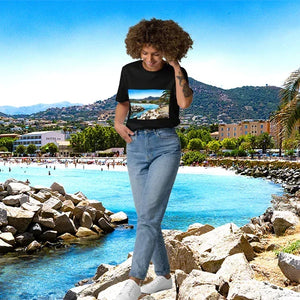 Woman in jeans and t-shirt with scenic beach print standing on rocks by a sunny coastal town
