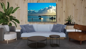 Modern living room with light blue sofa, potted plant, and wall art of boats on tranquil water at sunset.