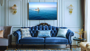 Elegant living room with blue tufted sofa, decorative pillows, and wall art of a boat at sea