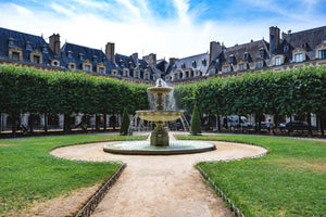 image représentant une fontaine, le jardin et les façades de la place des Vosges à Paris sous un ciel bleu